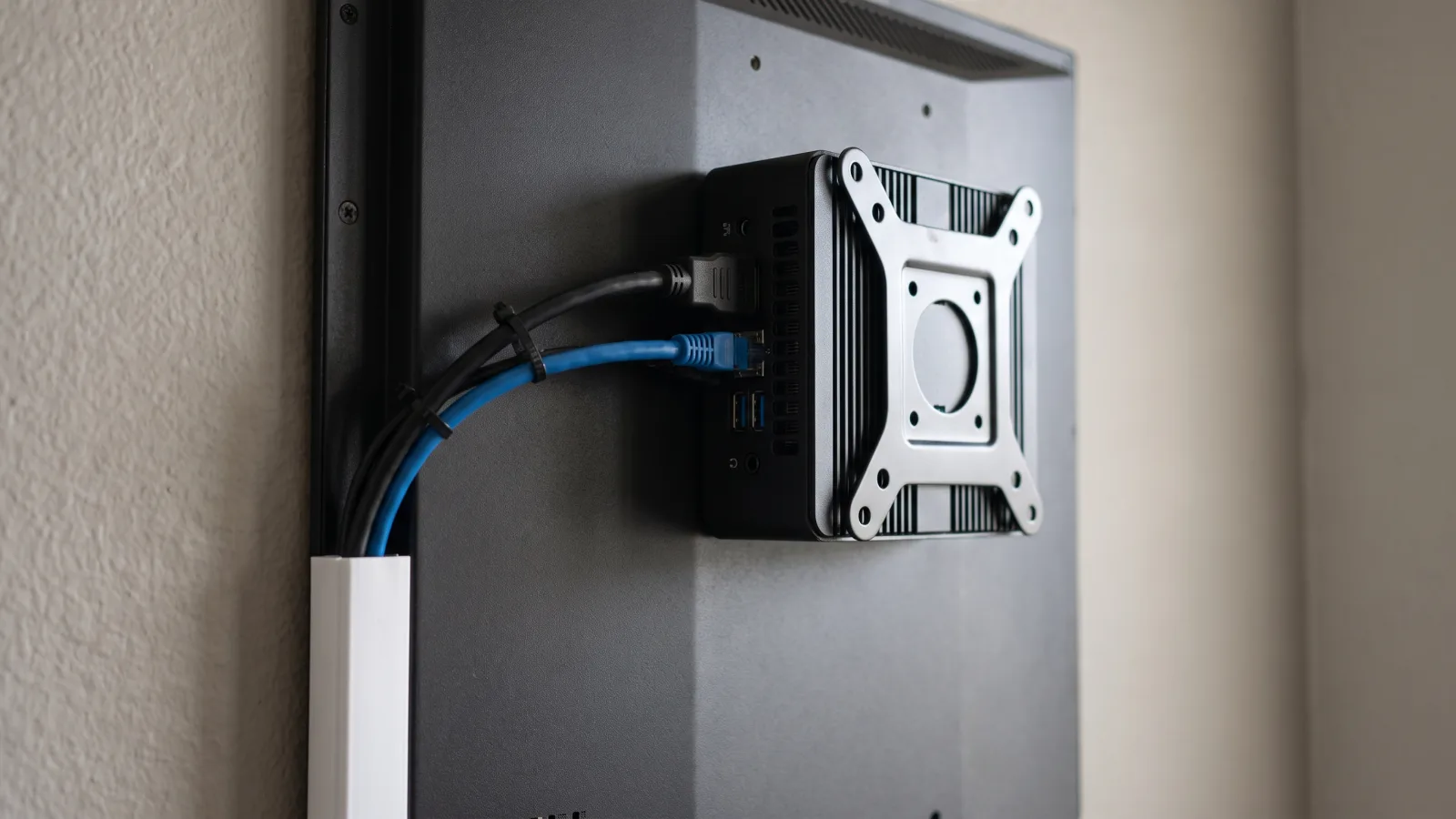Compact Windows mini PC mounted behind a commercial display with HDMI and Ethernet cables neatly routed