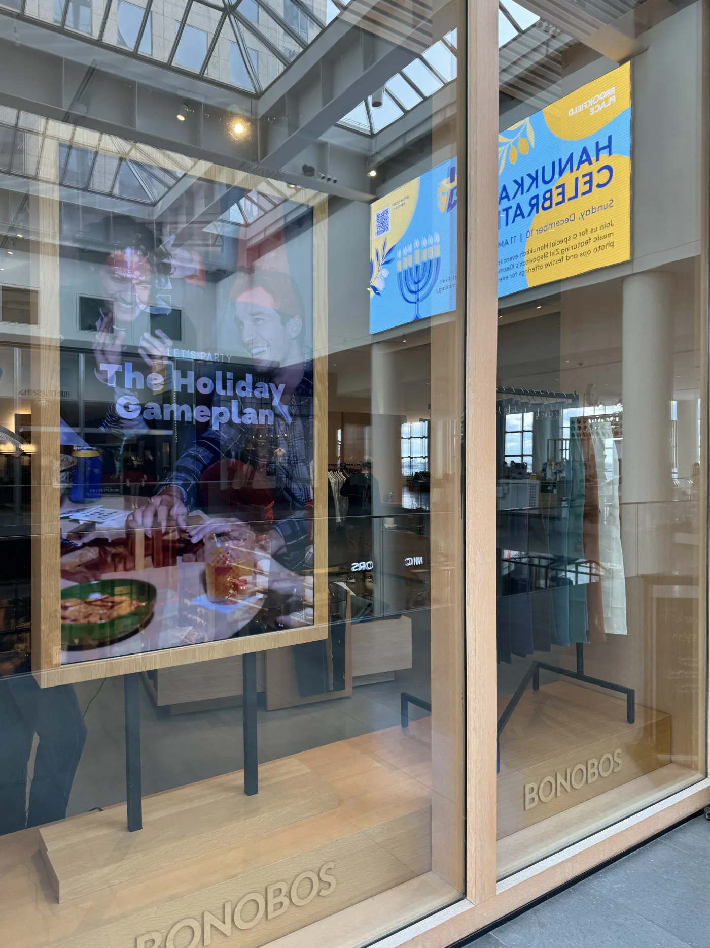 Bonobos storefront window — 'The Holiday Gameplan' display and digital Hanukkah celebration screen