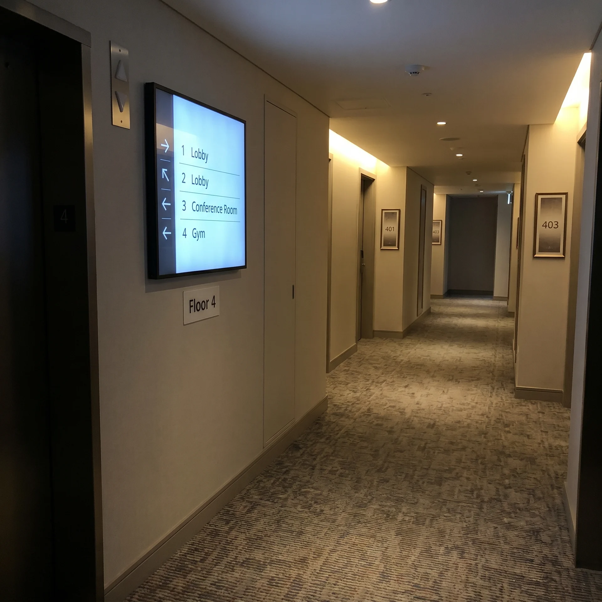 Hotel guest-floor hallway with multi-floor wayfinding screen — lobby, conference, and gym directional signage.