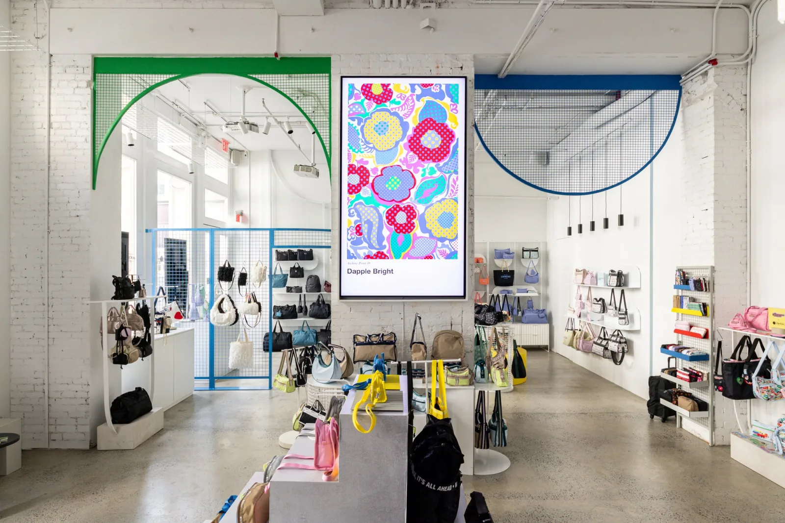 LeSportsac SoHo flagship sales floor with the 98-inch Samsung QM98C display showing the Dapple Bright floral campaign above the handbag tables