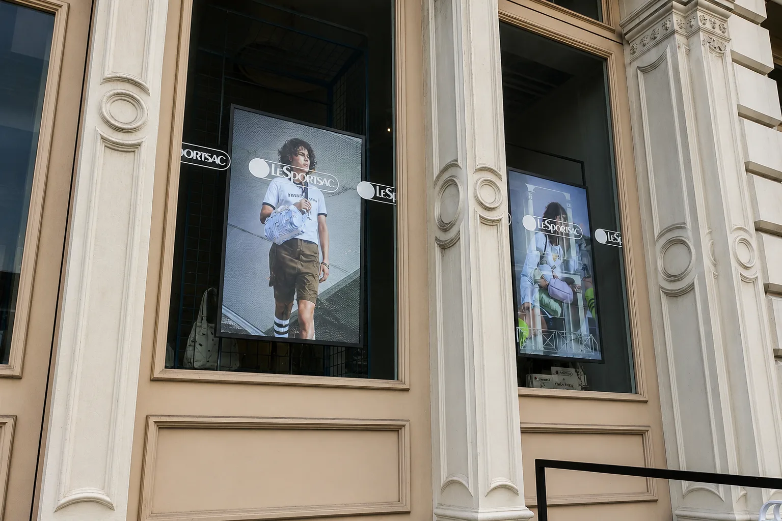 Angled street view of two LeSportsac window displays inside the SoHo storefront, set into the building's cast-iron facade