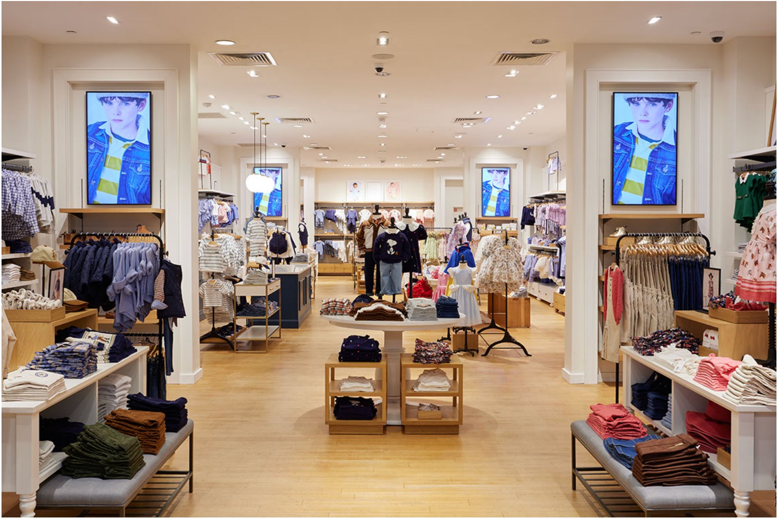 Four synchronized Samsung QM50C 4K displays mounted on columns in a Janie and Jack store interior