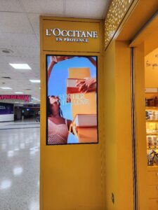 L’Occitane storefront corner with a tall vertical digital display showing a lifestyle promotional image.