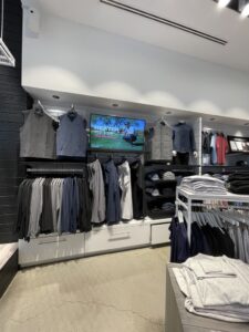 Retail apparel wall with a widescreen display above folded and hanging clothing.