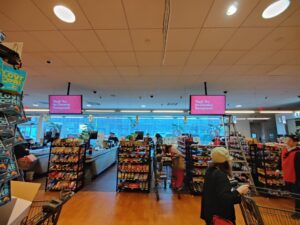 Large grocery checkout area with two hanging digital screens over the registers.