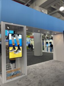 Trade show booth window frame featuring a vertical digital signage display showing a footwear ad.