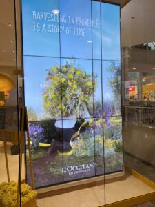 L’Occitane storefront with a large multi-panel video wall showing branded campaign imagery.