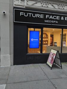 Future Face & Body MedSpa” storefront with a vertical digital screen in the window and an A-frame sign on the sidewalk.