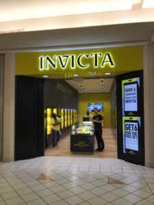 Invicta store entrance with a portrait digital sign promoting an in-store sale.
