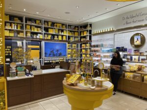 L’Occitane checkout area with large digital screen, shelving, and yellow merchandising.