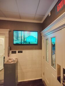 Funeral home lobby with wall-mounted screen showing a forest scene near doorway.