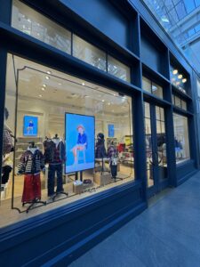 Angled view of storefront with large window digital signage and mannequins