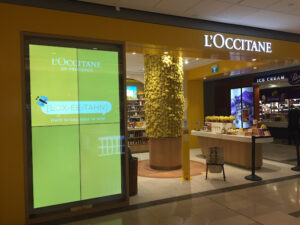 L’Occitane shop entrance with a large vertical digital screen showing promotional content.