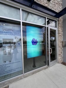 Dental office storefront with a vertical digital signage screen visible through the glass.