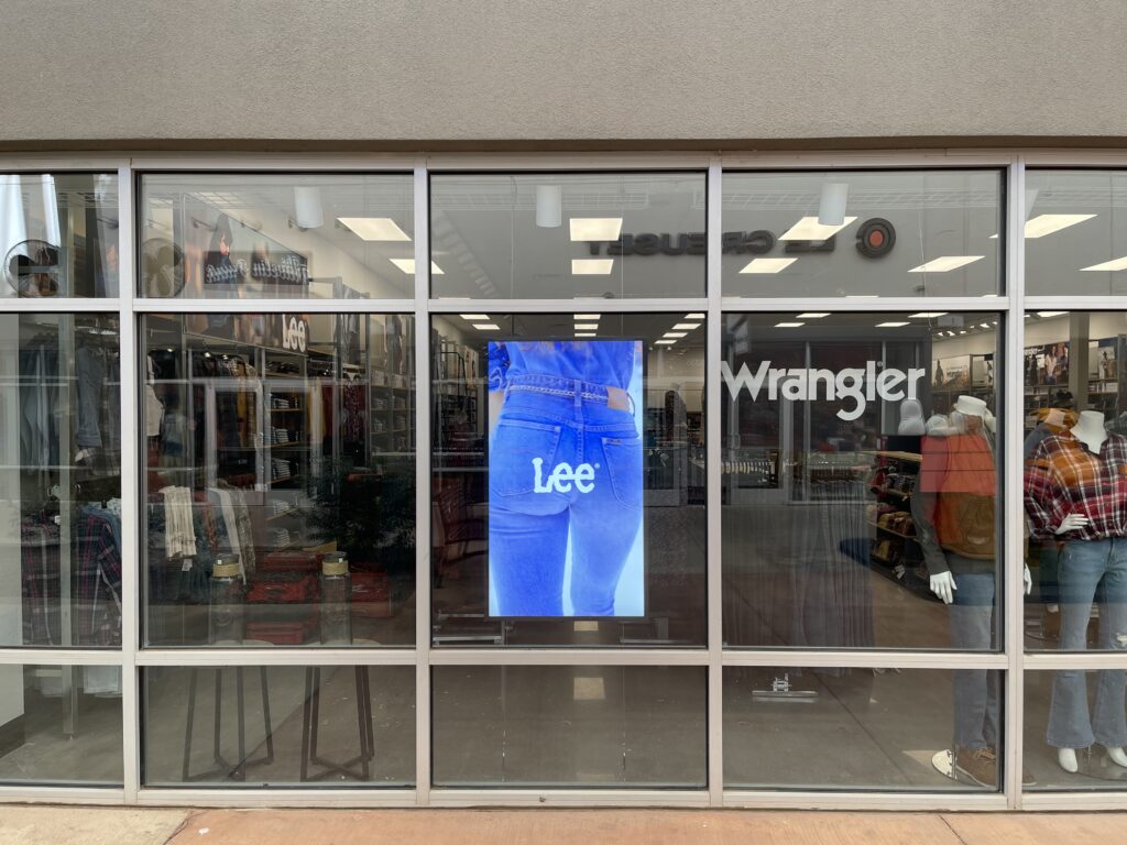 Wrangler storefront windows with a vertical digital sign showing a Lee jeans advertisement.