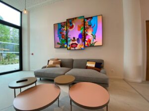Modern lounge with gray sofa, round tables, pendant lights, and three colorful wall-mounted screens.