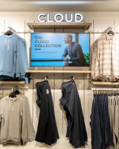 Retail clothing wall with a digital screen promoting the Cloud Collection above apparel racks.