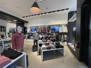 Modern apparel store interior with product tables and integrated digital displays in back.