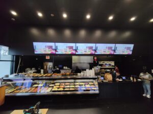 Five digital menu boards mounted above counter in modern food-service interior.
