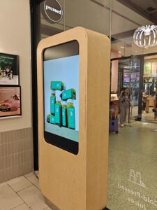 Freestanding indoor digital kiosk near entrance showcasing promotions and product visuals.