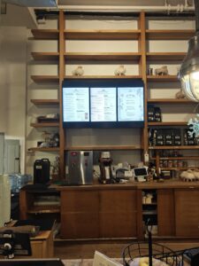 Three commercial displays mounted cleanly within custom wooden shelving, showing the café’s digital menu. A modern, minimal setup ideal for crowded NYC counter areas.