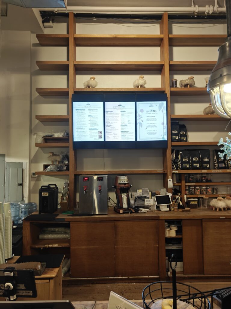 Three commercial displays mounted cleanly within custom wooden shelving, showing the café’s digital menu. A modern, minimal setup ideal for crowded NYC counter areas.
